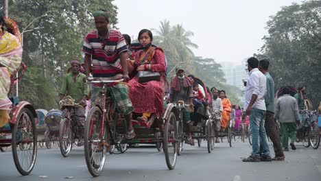 Cinematic-shot-of-Bangladeshi-commuters-riding-on-rickshaws-as-pedestrians-try-to-cross-a-busy-road-in-Dhaka