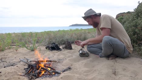 A-coastal-survival-man-eating-fish-on-a-camp-fire-by-the-ocean
