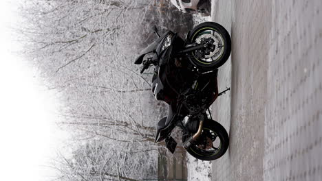 Vertical-video-of-a-black-Kawasaki-Ninja-650-motorcycle,-parked-on-a-snowy-landscape