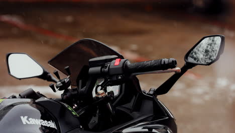 Handlebar-and-mirrors-details-of-a-black-Kawasaki-Ninja-650,-on-a-snowy-day