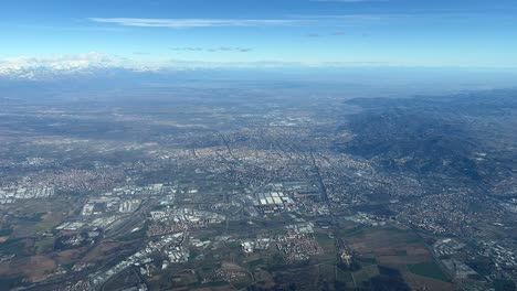 Vista-Aérea-De-La-Ciudad-De-Turín-En-El-Norte-De-Italia,-Junto-A-Los-Alpes-Italianos-Nevados-En-Una-Espléndida-Y-Soleada-Mañana-De-Invierno-Grabada-Desde-Una-Cabina-De-Jet-Que-Sale-Del-Aeropuerto