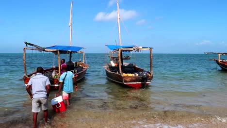 Verankerte-Tansanische-Boote-Schwanken-Am-Meeresufer,-Während-Die-Einheimischen-Vorräte-Laden
