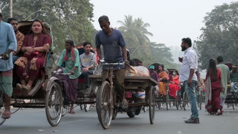 Zeitlupenaufnahme-Von-Bangladeschischen-Pendlern,-Die-Auf-Rikschas-Fahren,-Während-Fußgänger-Versuchen,-Eine-Stark-Befahrene-Straße-In-Dhaka-Zu-überqueren