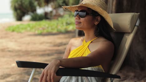 Asian-Woman-Sitting-On-A-Beach-Chair-Wearing-Summer-Hat