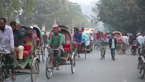 Zeitlupenaufnahme-Von-Bangladeschischen-Fußgängern-Und-Pendlern,-Die-Auf-Rikschas-Auf-Einer-Stark-Befahrenen-Straße-In-Dhaka-Fahren