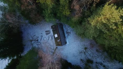Aerial-drone-top-down-shot-over-a-small-cottage-in-the-middle-of-woods-with-thin-layer-of-snow-covered-on-a-cold-winter-day
