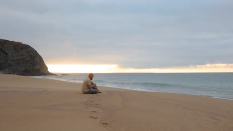 Un-Hombre-Sentado-Y-Bebiendo-Café-Matutino-Mientras-Observa-El-Amanecer-En-Una-Playa-Aislada-En-Australia