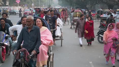 Zeitlupenaufnahmen-Von-Pendlern-Aus-Bangladesch,-Die-Auf-Rikschas-Fahren,-Während-Fußgänger-Die-Straße-Teilen