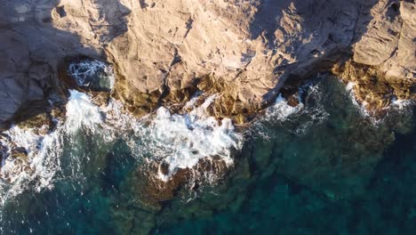 Sideways-background-aerial-view-of-waves-crashing-against-rocks,-turquoise-water,-Sardinia,-Italy,-summer-vacation-travel-destination