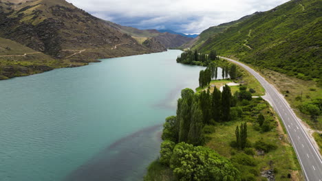 A-drone-shot-made-above-an-asphalt-road-and-a-walking-trail-winding-along-the-fiord-nearby-the-Champagne-Gully-Freedom-Camping,-New-Zealand