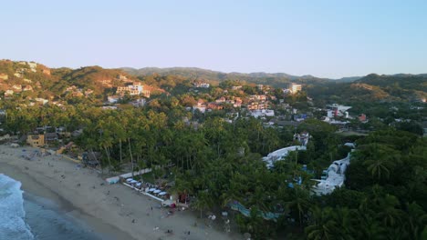 Eine-Drohne-Fliegt-Bei-Sonnenuntergang-über-Den-Strand-Und-In-Richtung-Der-Surferstadt-Sayulita-Mexico