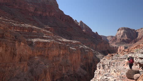 Lonely-Female-Hiker-With-Backpack-in-Grand-Canyon-National-Park-Walking-on-Red-Rocks-Above-Abyss,-Slow-Motion