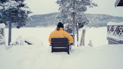 Mann-In-Gelber-Jacke-Sitzt-Mit-Seinem-Hund-Alaskan-Malamute-Vor-Dem-Schneebedeckten-Hof