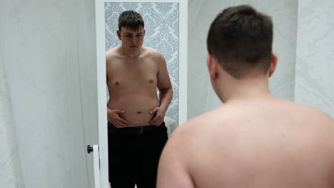 Sad-Young-Fat-Man-Standing-in-Front-of-Mirror-Looking-at-His-Big-Belly,-Slow-Motion