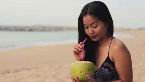 Chica-Tailandesa-De-Pelo-Largo-Está-Bebiendo-Jugo-De-Fruta-De-Palma-Fresca-En-La-Orilla