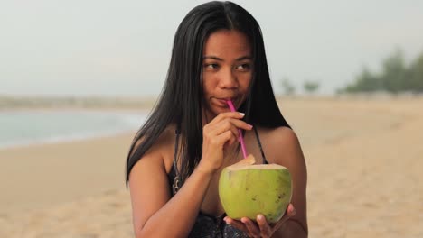 Junge-Asiatische-Frau-Trinkt-Am-Strand-Eine-Gesunde-Natürliche-Kokosnuss-Erfrischung