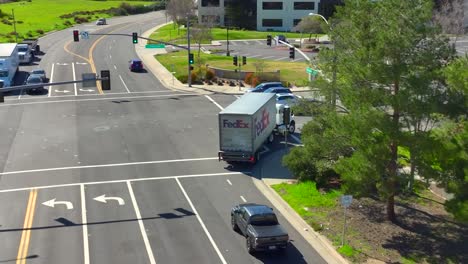 Aerial-view-following-FEDEX-truck-driving-through-bright-sunny-city-turning-at-junction-to-deliver-parcel