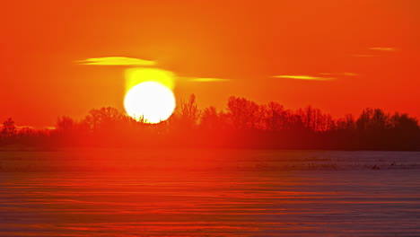 Time-lapse-of-blinding-sun-rising-in-golden-sky-over-snowy-landscape