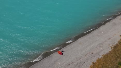 Drone-overhead-view---wing-foil-surfing-gear-on-lake-shore,-brilliant-blue-water