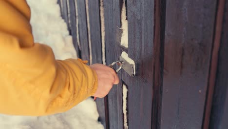 Man-Unlocking-Frozen-Padlock-Of-Wooden-Gate-In-Winter