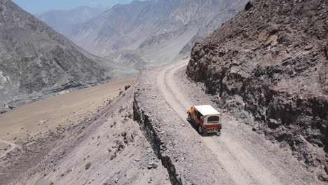 Entdecken-Sie-Pakistan,-Luftaufnahme-Eines-Geländewagens-Auf-Einer-Unbefestigten-Straße-Am-Hang-Oberhalb-Des-Canyons,-Verfolgungsdrohnenaufnahme