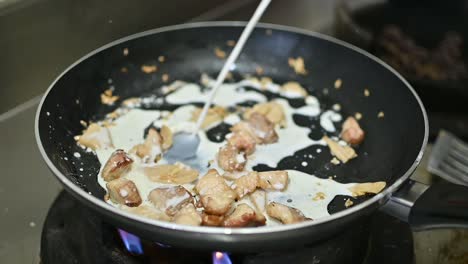 White-Cream-Sauce-Being-Poured-Over-Cut-Meat-Pieces-In-Frying-Pan