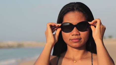 Eine-Frau,-Die-An-Einem-Sonnigen-Sommertag-Am-Strand-Steht,-Trägt-Zum-Schutz-Eine-Sonnenbrille