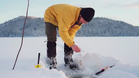 Man-Bending-Down,-Uses-Bait-In-Fishing-Rod-To-Catch-Fish-In-Ice-Hole