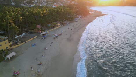 A-drone-flys-overhead-of-the-Sayulita-beach-towards-the-setting-sun-in-Mexico