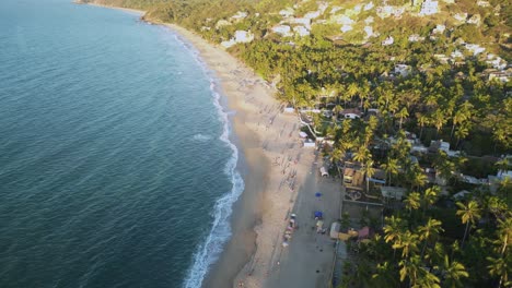 The-beach-at-Sayulita,-Mexico-has-people-sun-tanning-and-walking-along-the-shore-as-seen-from-a-drones-point-of-view