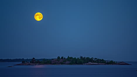 The-full-moon-setting-over-a-islet-in-a-calm-sea---nighttime-time-lapse