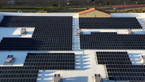 Solar-panels-installation-on-commercial-building-rooftop-rising-aerial-view-to-reveal-busy-highway-traffic