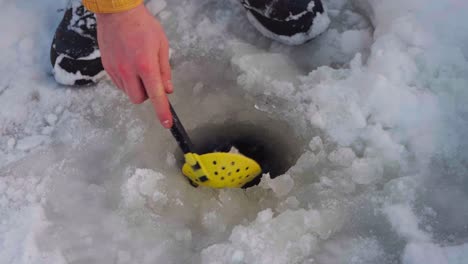 Man-Scooping-Ice-From-The-Fishing-Hole-On-The-Frozen-Lake-By-Ice-Skimmer-Scoop