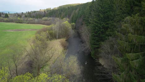 Drone-flies-fast-over-Slovakian-river,-pine-forest-and-meadow