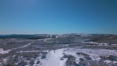 Aerial-view-of-a-winter-and-snowy-landscape-with-roads,-mountains-on-the-horizon-and-a-person-walking-on-the-ground