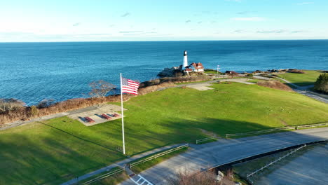 National-flag-of-the-United-States-of-America-gently-flutters-in-the-wind-with-in-the-background-the-historical-Portland-head-light-house-on-a-sunny-day