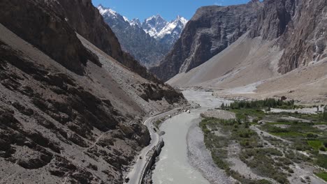 Aerial-View-of-Road-and-Glacial-River-in-Highlands-of-Pakistan,-Hunza-Valley-on-Sunny-Summer-Day,-Drone-Shot