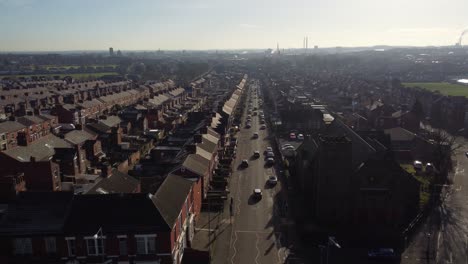 Aerial-view-across-terraced-houses-and-a-long-road-leading-towards-the-bustling-town-centre,-establishing-street-scene-shot