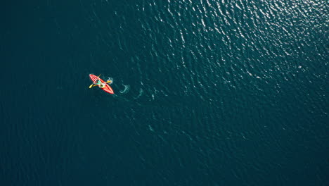 High-top-down-aerial-of-two-people-paddling-orange-kayak-in-wavy-water