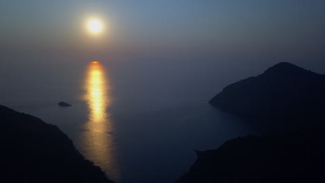 Rich-gold-and-blue-ocean-sunset,-seen-from-mountain-island-aerial