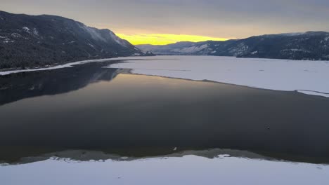 Dramatic-Sunset-over-Little-Shuswap-Lake-in-Winter,-Snow-Covered-Ground-Surrounded-by-Evergreen-Trees,-Aerial-View