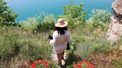 Back-View-Of-A-Woman-Going-Down-The-Steep-Stairs-With-Poppy-Flowers-In-Kaliakra,-Bulgaria