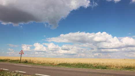 Cielo-Azul-Nublado-Sobre-La-Carretera-Y-El-Campo-Agrícola---Lapso-De-Tiempo