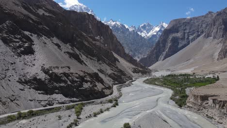 Valle-De-Hunza,-Pakistán,-Vista-Aérea-De-La-Ruta-Escénica-Por-El-Agua-Del-Río-Glacial-Bajo-Los-Picos-De-Las-Montañas-Cubiertas-De-Nieve