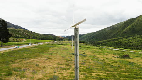 Old-windmill,-road-and-green-vibrant-valley-of-Central-Otago-in-New-Zealand,-aerial-orbit-view