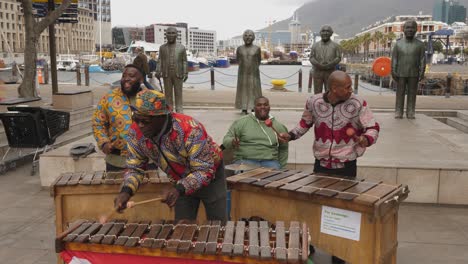 African-men-perform-on-marimbas-by-Nobel-Square,-Cape-Town-statues