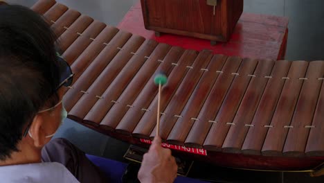 Over-shoulder-view,-Asian-man-playing-wooden-ranat-thai-xylophone-using-mallets,-Thailand