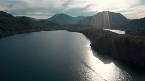 Wide-forward-aerial-of-lake-and-mountains-in-Argentina,-lens-flare