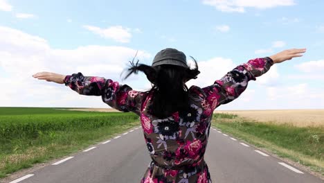 Una-Mujer-Feliz-Sintiendo-El-Aire-Mientras-Camina-Por-Una-Carretera-Rural-Vacía