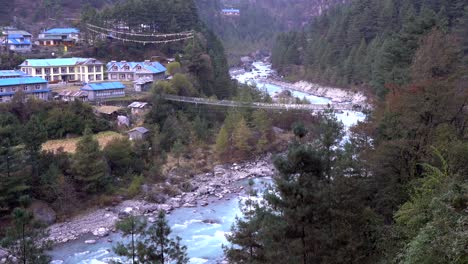A-glacier-river-winding-its-way-through-a-valley-bordered-by-rugged-mountains-with-a-swinging-bridge-over-the-river
